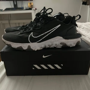 Nike reacts vision  - Snygga svarta Nike sneakers med vit sula och den ikoniska swoosh-loggan i vitt. Skorna har snörning och en modern design som passar perfekt för en sportig look.