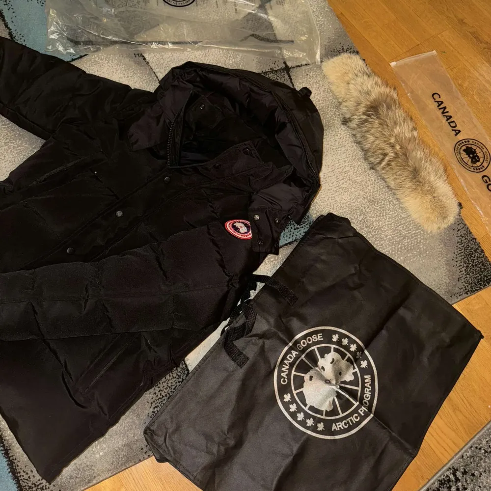 Säljer en svart dunjacka från Canada Goose med avtagbar pälskant på huvan. Jackan har en broderad logotyp på ärmen och stängs med både dragkedja och knappar. Perfekt för kalla vinterdagar. 10/10 skick med alla tags och påse kommer med!. Takit.