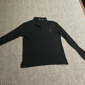 Svart långärmad pikétröja från Ralph Lauren - Snygg svart långärmad pikétröja/rugbytröja från Ralph Lauren med klassisk krage och knappdetaljer. Perfekt för en stilren look. Är i storlek s men sitter lite litet, slimfit. Nypris : 1300 
