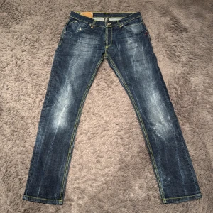 Blå jeans Dondup slim fit - Snygga blå jeans med gul kontrastsöm och slitna detaljer. Dondup jeans med en Klassisk femficksdesign med knappgylf och bälteshällor. Perfekta för en avslappnad stil. Dessa är eftertraktade och väldigt många är intresserade!       Storlek 33/M