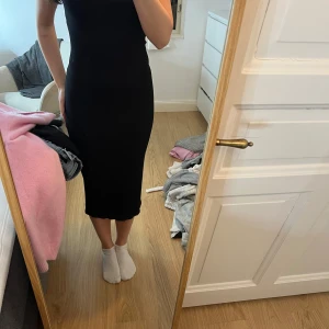 Svart ribbad klänning med öppen rygg - Snygg svart ribbad klänning med en stilren design och öppen rygg. Klänningen har en tight passform och slits baktill för extra stil. Perfekt för en kväll ute eller en speciell tillställning.