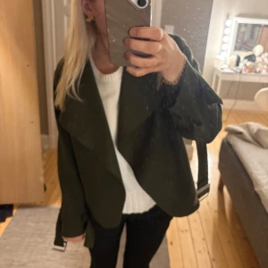 Olivgrön jacka med draperad krage - Snygg olivgrön jacka med en draperad krage och långa ärmar. Perfekt för höst och vår, den har en loose passform som ger en avslappnad look. Jackan är tillverkad i ett mjukt material som känns bekvämt att bära.