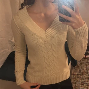 Beige stickad tröja  - Säljer en snygg beige stickad tröja från Hilfiger Denim. Tröjan har en v-ringad design med kabelstickade detaljer och långa ärmar. Använt ett fåtal gånger 🫶