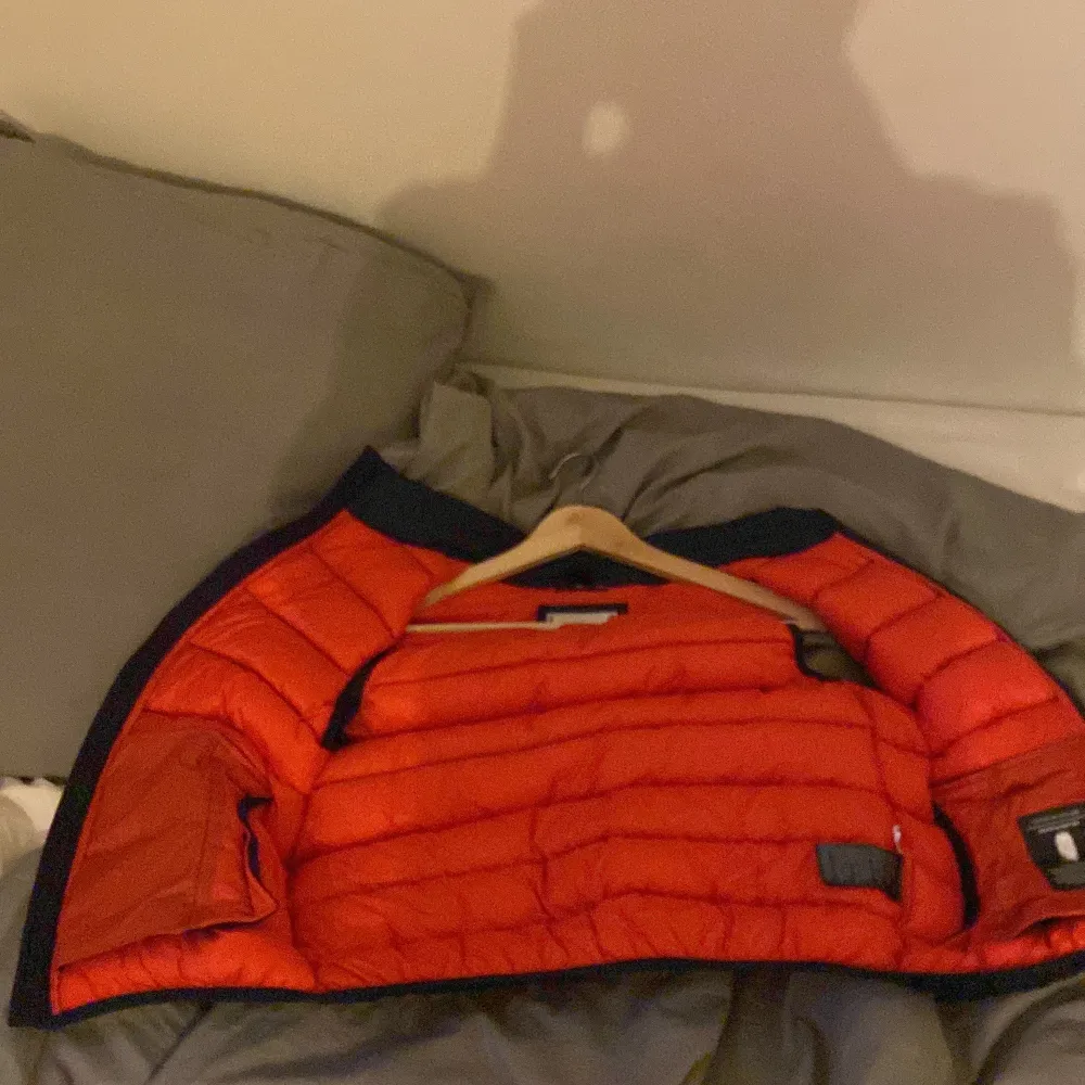 Snygg mörkblå dunväst från Tommy Hilfiger dragkedja och orange foder. Västen har en broderad logga på kragen och praktiska fickor framtill. Perfekt för varmare vår dagar när du vill hålla stilen. I storlek 164.. Takit.