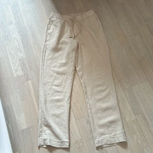 Beige linnebyxor från A Day's March - Snygga beige linnebyxor från A Day's March med rak passform. Endast använda ett fåtal gånger och är som nyskick. Storlek 48 och skulle passa någon som är ca 180 lång. 