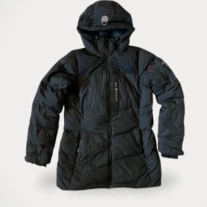 sail racing patrol down jacket dam w dunjacka dun vinterjacka parka parkas vinter down - Säljer en svart dunjacka från Sail racing med huva och dragkedja. Jackan har en stilren design och är perfekt för kyliga dagar. Den har långa ärmar och en logotyp på bröstet. Passar bra för vintersäsongen.