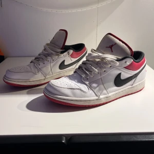 Nike Air Jordans i vitt och rött - Snygga Nike Air Jordans i vitt med röda och svarta detaljer. Skorna har klassisk snörning och en ikonisk design med Jumpman-logga på plösen. Perfekta för dig som vill ha en stilren och sportig look.