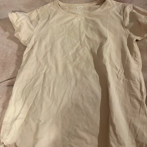 Beige t-shirt från 157 - Säljer en enkel och stilren beige t-shirt från 157. Den har korta ärmar och en rund halsringning, perfekt för en avslappnad look. T-shirten är gjord i ett mjukt material som känns skönt mot huden.