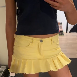 Gul kortkjol med volang - Snygg gul kortkjol med volangdetaljer. Kjolen har en klassisk jeansstil med fickor och knappstängning. Perfekt för en solig dag! Sytt den själv från gula jeans.