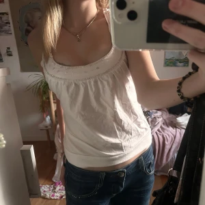 Vit ärmlös topp med pärldetaljer - Säljer en söt vit ärmlös topp med pärldetaljer längs halsringningen. Toppen har dubbla axelband och en lätt rynkad design framtill. Party topp så att säga! Skriv för fler bilder! 🤍