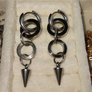 Örhängen med ringar och koner - Snygga örhängen i silver med flera ringar och en hängande konformad detalj. Perfekta för att ge en edgy touch till din outfit. De har en modern och unik design som verkligen sticker ut.