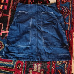 Blå jeanskjol från Arket - Säljer en snygg blå jeanskjol från Arket med fickor fram och dragkedja bak. Kjolen har en klassisk A-linjedesign. I bomull. Storlek 34.