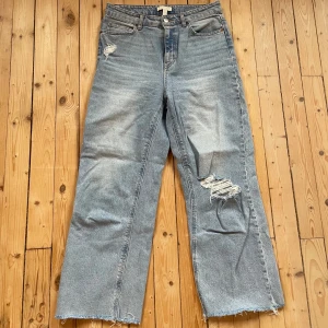 Blå jeans med slitningar - Snygga blå jeans med slitningar från H&M. De har en hög midja och raka ben. Slutar vid ankeln på mig som är 172cm lång. Använda några gånger men i mycket gott skick. 99% bomull 1% elastan.