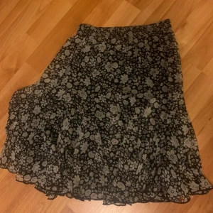 Blommig kjol från Capri Collection - Säljer en söt blommig kjol från Capri Collection i svart och grått. Storlek xs.