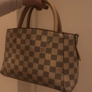 Rutig handväska - Snygg handväska med klassiskt rutigt mönster i beige och brunt. Väskan har två handtag och en stilren design som passar perfekt för alla tillfällen. Den är rymlig och praktisk för att bära med sig det viktigaste.