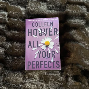 All Your Perfects - Säljer boken 'All Your Perfects' av Colleen Hoover. Omslaget är lila med en vit prästkrage i mitten. Perfekt för dig som gillar romantiska och känslosamma berättelser. En riktig bladvändare!