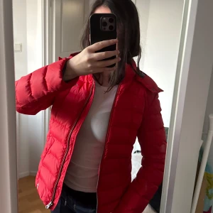 Röd dunjacka från Tommy Hilfiger - Säljer en snygg röd dunjacka från Tommy Hilfiger. Jackan har en dragkedja framtill och långa ärmar. Den har en liten logotyp på bröstet och en hög krage för extra skydd mot vind samtidigt som den är väldigt skön!