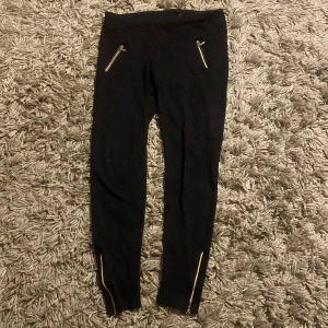 Svarta mjukis leggings med dragkedjor - Snygga svarta mjukis leggings från My His Woman med dragkedjor framtill och vid bensluten. Perfekta för en stilren look med en touch av edge. De är stretchiga och bekväma, vilket gör dem till ett utmärkt val för både vardag och speciella tillfällen.