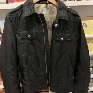 Svart jacka från J.Lindeberg - Snygg svart jacka från J.Lindeberg med dragkedja och knappar. Den har en klassisk krage och två bröstfickor med knappstängning. Perfekt för en stilren look. Står att det är en storlek S men passar XS   Skriv om frågor