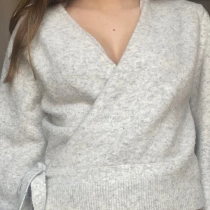 Grå omlottkofta från & Other Stories - Säljer en stilren grå omlottkofta från & Other Stories. Koftan har en knytning i sidan och är perfekt för lager-på-lager. Den är tillverkad i ett mjukt material och har långa ärmar. Passar utmärkt för både höst och vår.