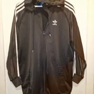 Svart jacka från Adidas - Säljer en svart jacka från Adidas med mesh see thrue tyg längs ärmarna. Perfekt för sportiga aktiviteter eller en avslappnad stil där du vill sticka ut. Garderobsrensning så kika gärna på övriga auktioner.