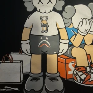 Kaws x supreme - Säljer en svart t-shirt med ett unikt konstmotiv av två figurer, en stående och en sittande. Designen är i grått, vitt och beige med detaljer som shoppingpåsar och sneakers. Perfekt för den som gillar streetwear och konst.