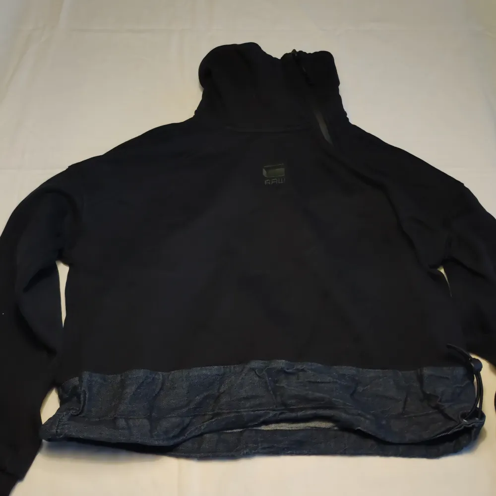 Säljer en svart jacka från G-Star RAW med huva och denimdetaljer vid nederkanten. Jackan har en stilren design med långärmade ärmar och en liten logotyp på framsidan. Perfekt för en casual look.. Takit.