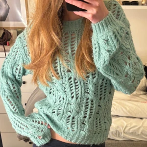 Mintgrön stickad tröja - Säljer en mysig mintgrön stickad tröja med ett öppet stickmönster. Tröjan har långa ärmar och ribbade muddar vid ärmslut och nederkant. Perfekt för kyliga dagar!