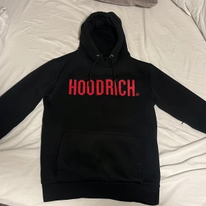 Svart hoodie Hoodrich - Säljer en svart hoodie från Hoodrich med röd text på framsidan. huva och ficka i armen samt en stor ficka framtill. Nypris:1000kr. Pris kan diskuteras