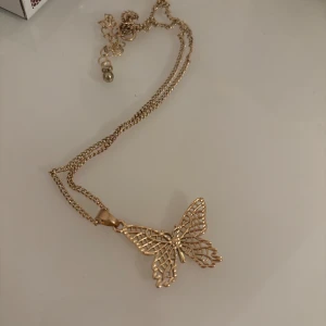 Guldigt fjärilshalsband - Elegant halsband i guld med ett detaljerat fjärilshänge. Kedjan är tunn och smidig, vilket ger en stilren look. Perfekt för att lägga till en touch av elegans till din outfit. Knappt använd!