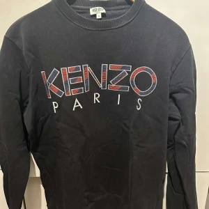 Svart tröja från Kenzo - Säljer en svart tröja från Kenzo med färgglatt broderat logotyp på framsidan. Tröjan har långa ärmar och en rund halsringning. Perfekt för en stilren och modern look.