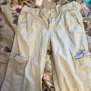 Beige cargobyxor från H&M - Säljer ett par beige cargobyxor från H&M i storlek EUR 152. Byxorna har flera praktiska fickor och är tillverkade i 100% bomull, vilket gör dem bekväma och slitstarka. Perfekta för en avslappnad stil.