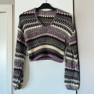 Mönstrad stickad tröja  - Säljer en cool stickad tröja från Pull&bear i grönt, lila och vitt. Tröjan är croppad med ett unikt mönster och har långa ärmar. Mycket älskad av mig men förtjänar ett nytt hem.