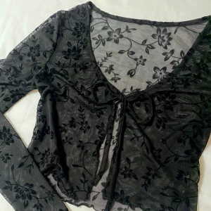 Svart blommig mesh topp - Snygg svart mesh topp med blommigt mönster och knytning framtill. Perfekt för att göra din outfit intressant och unik. Kontakta om du har frågor☺️