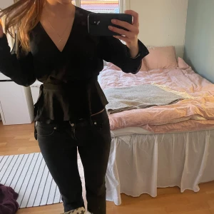 Svart omlottopp - Säljer en elegant svart omlottopp med v-ringning och långa ärmar. Perfekt för att klä upp eller ner beroende på tillfälle.