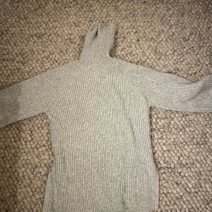 Grå ribbad polotröja från Gina Tricot - Säljer en stilren grå ribbad polotröja från Gina Tricot. Tröjan har långa ärmar och en hög polokrage som håller dig varm under kyliga dagar. Perfekt för lager-på-lager eller som den är. Passar utmärkt till både jeans och kjol.