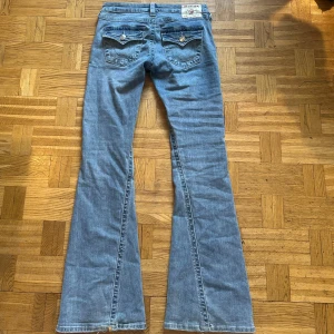 Blå jeans från True Religion - Ett par sjukt snygga bootcut och lowwaist byxor från true religion!!💗 de har liten slitning på en hälen: se bild. Säljer då de inte är min stil längre. Mått: 38cm rakt över midjan, 81cm innerbenslängd, 102cm full längd, 19cm grenhöjd och 27cm benöppning. Det är bara o fråga ifall du undrar över något!