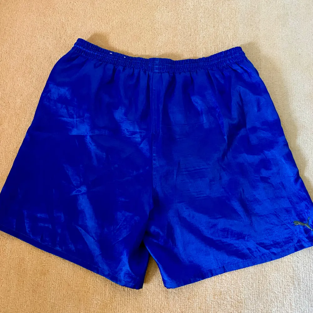 Sköna Puma shorts i glansigt material, stl XL. Bra skick, endast små tecken på användning. Stor tryckt logga och en broderad logga på benen.. Shorts.