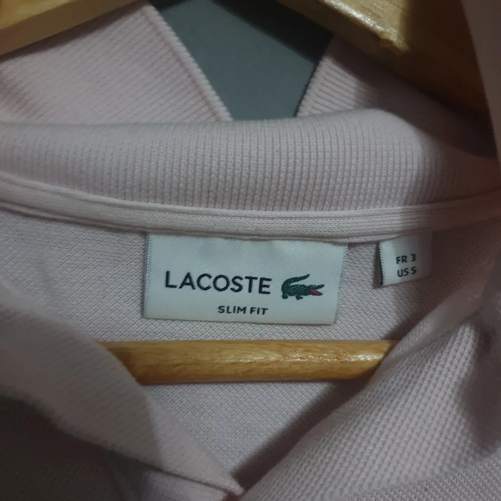 Säljer en stilren ljusrosa pikétröja från Lacoste. Den har en klassisk krage och korta ärmar, perfekt för en avslappnad men ändå snygg look. Tröjan är i slim fit och har den ikoniska Lacoste-loggan på bröstet. Perfekt för vår och sommar!. Tröjor & Koftor.