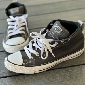 Grå Converse All Star sneakers - Säljer ett par klassiska grå Converse All Star sneakers i storlek herr 42. De har en snygg och tidlös design med vit snörning och vit tåhätta. Skorna är tillverkade i textil med en gummisula, perfekta för både vardag och fest. De är i bra skick och