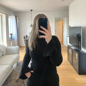 Tröja  - Svart långärmad tröja med trumpet ärmar i ett ribbat material 