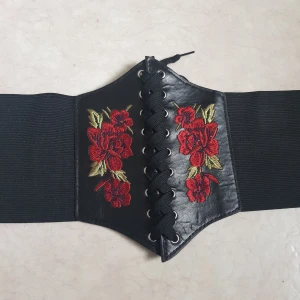 Svart bälte med blombroderi - svart bälte/korsett med broderade röda rosor, snörning framtill och elastiskt material för en bekväm passform. Sliten vid knapparna bak, en liten liten tråd sticker ut på framsidan.