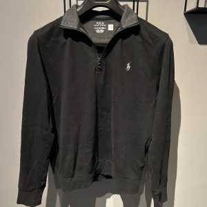 Svart tröja med dragkedja från Polo Ralph Lauren - Säljer en stilren svart tröja från Polo Ralph Lauren i storlek XS. Tröjan har en halv dragkedja framtill och den klassiska loggan broderad på bröstet. Perfekt för både vardag och lite finare tillfällen. Den är i nyskick och superbekväm att ha på sig!