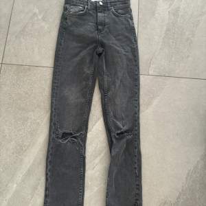 Säljer ett par mörk gråa  jeans med coola slitningar på knäna. De är högmidjade och har en straight/lite utsvängda passform. Passar dig som är mellan 1’56-160cm