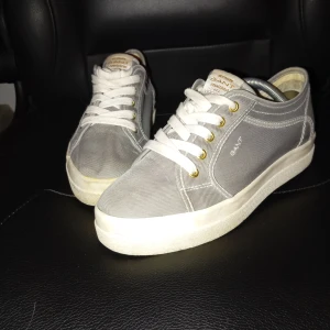 Grå sneakers från Gant - Säljer ett par stilrena grå sneakers från Gant. De har en klassisk design med vita snören och en vit sula. Perfekta för vardagsbruk och passar till det mesta i garderoben. Skorna är i bra skick och redo för en ny ägare!