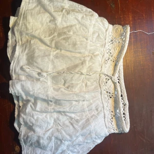 Vit kjol med spetsdetaljer - Säljer en superfin vit kjol med vackra spetsdetaljer i midjan. Kjolen har en lös passform och är perfekt för sommardagar. Den är gjord i ett lätt och luftigt material, vilket gör den bekväm att bära. Perfekt för en avslappnad dag på stranden eller en sommarfest! 🌞