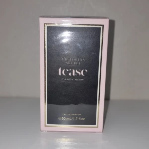 Tease Candy Noir Eau de Parfum - Upplev lyx med Victoria's Secret Tease Candy Noir, en exklusiv parfym som kombinerar elegans och förförande dofter. Denna parfym levereras i en stilfull rosa och svart förpackning, prydd med sofistikerade gulddetaljer som ger en känsla av tidlös glamour. Doften är en oemotståndlig blandning av söta noter från hallonglasyr, mystik från nattblommande iris och den varma, mjuka basen av tonkaböna – perfekt för en utekväll eller när du vill känna dig extra speciell.  Flaskan rymmer 50 ml, vilket gör den till den perfekta storleken att bära med sig i väskan för att fräscha upp sig när som helst. Produkten är helt ny och levereras i sin originalförpackning, fortfarande inslagen i skyddande plast för att säkerställa att den är i perfekt skick när du får den. Denna parfym är inte bara en doft, utan ett statement – ett måste för den moderna kvinnan som vill utstråla självförtroende och elegans.