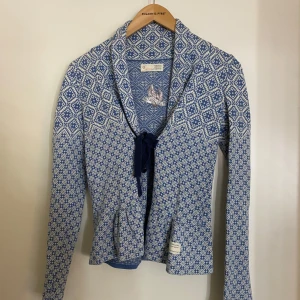 Blå mönstrad kofta från Odd Molly st 0 - Säljer en superfin blå och vit mönstrad kofta från Odd Molly. Den har långa ärmar och ett snyggt knytband framtill. Perfekt till alla tillfällen. Den har sitt unika mönster och broderade detalj på ryggen. Koftan är i nyskick och passar perfekt för en stilren look eller matcha till jeans och njuta av den sköna kvaliteten. St 0 vilket motsvarar XS men denna kan användas som S också. 