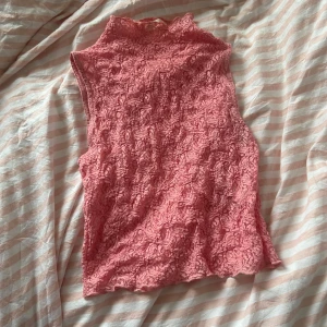 Rosa spetslinne - Säljer ett supersött rosa spetslinne i ett mjukt och stretchigt material. Linnet är ärmlöst och har en hög hals som ger en elegant touch. Passar perfekt till både jeans och kjol!