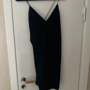 Svart axelbandslös klänning - Snygg svart klänning med smala axelband och v-ringad design. Perfekt för en utekväll eller fest. Klänningen har en elegant och enkel stil som passar till många tillfällen.